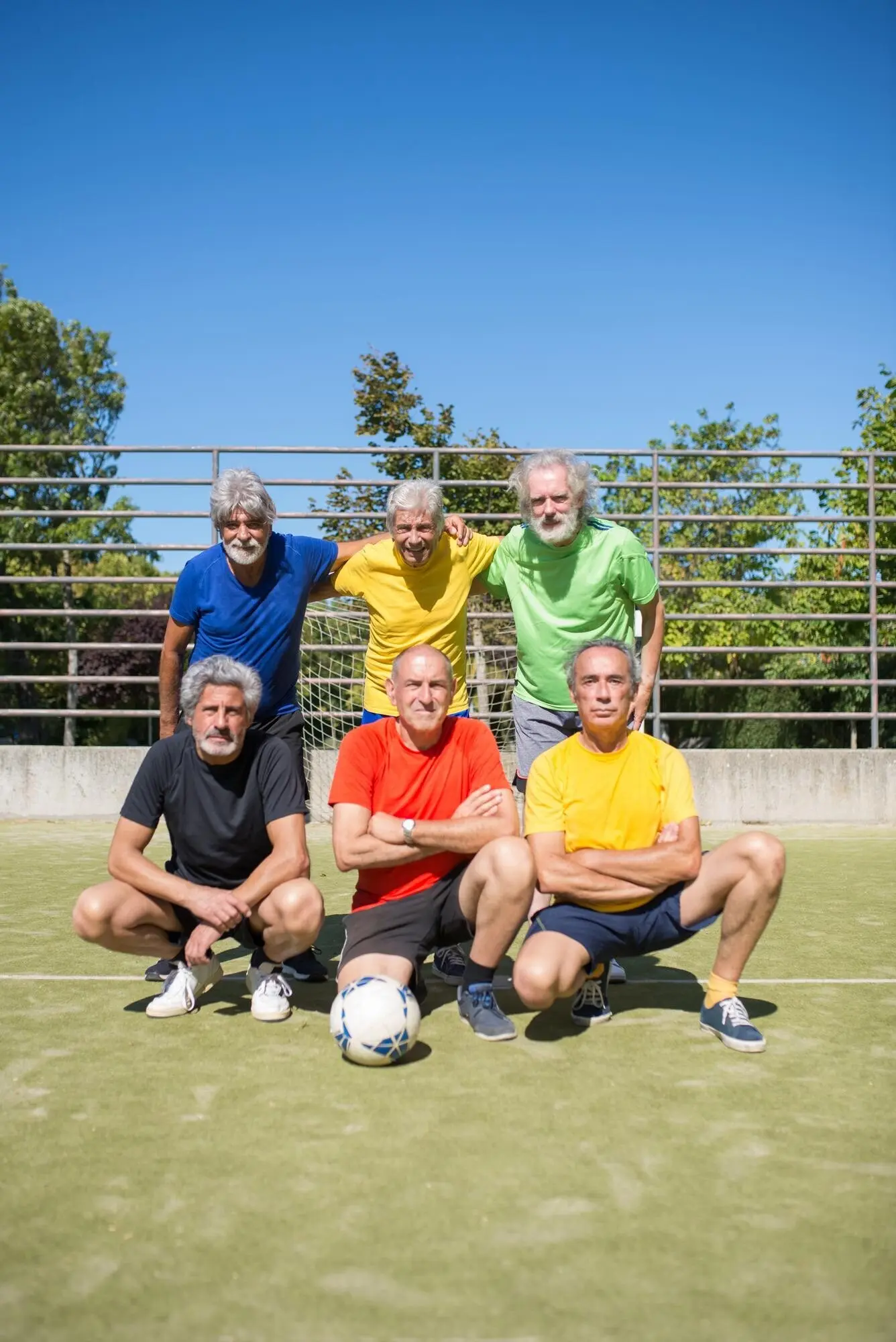 Portrait of happy senior men on the field before a match. Gray-haired men in sports clothing, standing and sitting, looking at the camera and posing. Football, sport, leisure concept.